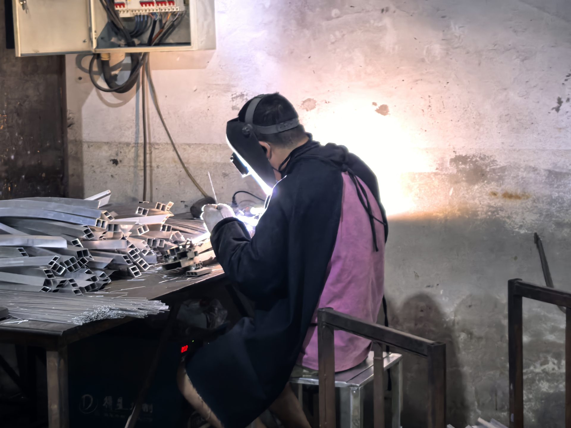 Worker welding an aluminium furniture frame, sparks flying